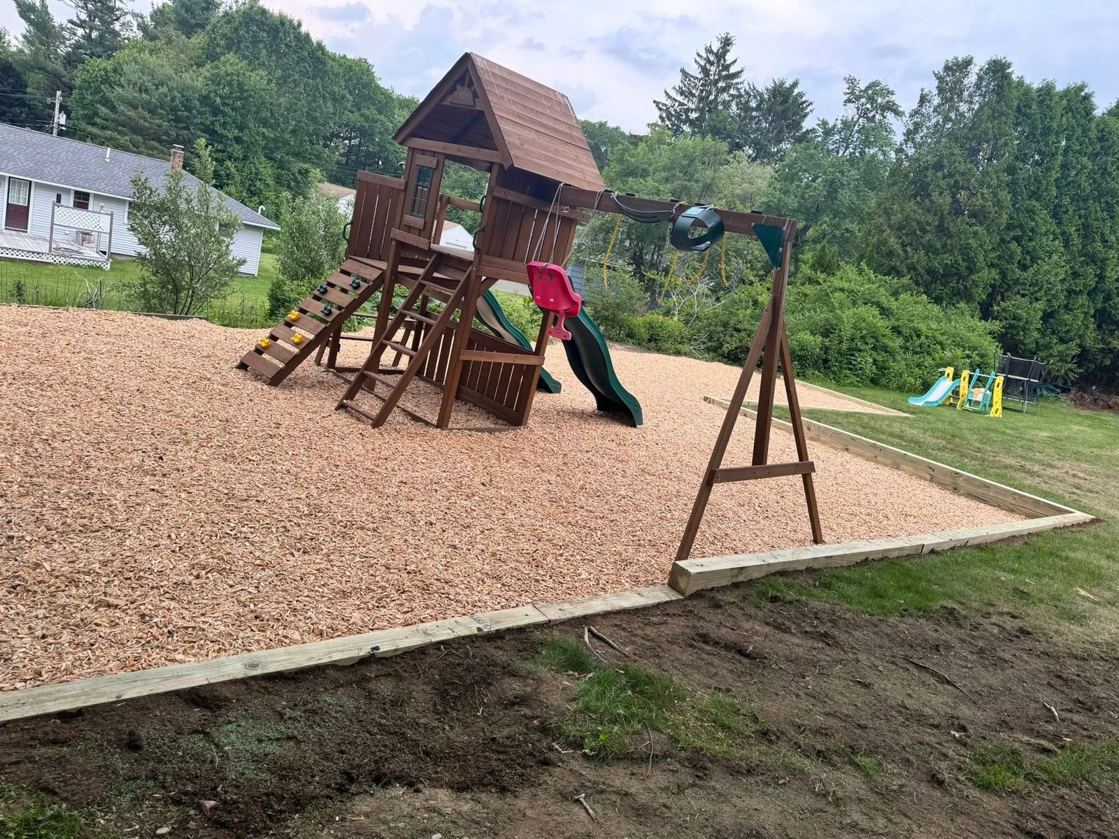 Wooden playset on a wood-chip play area with a timber border