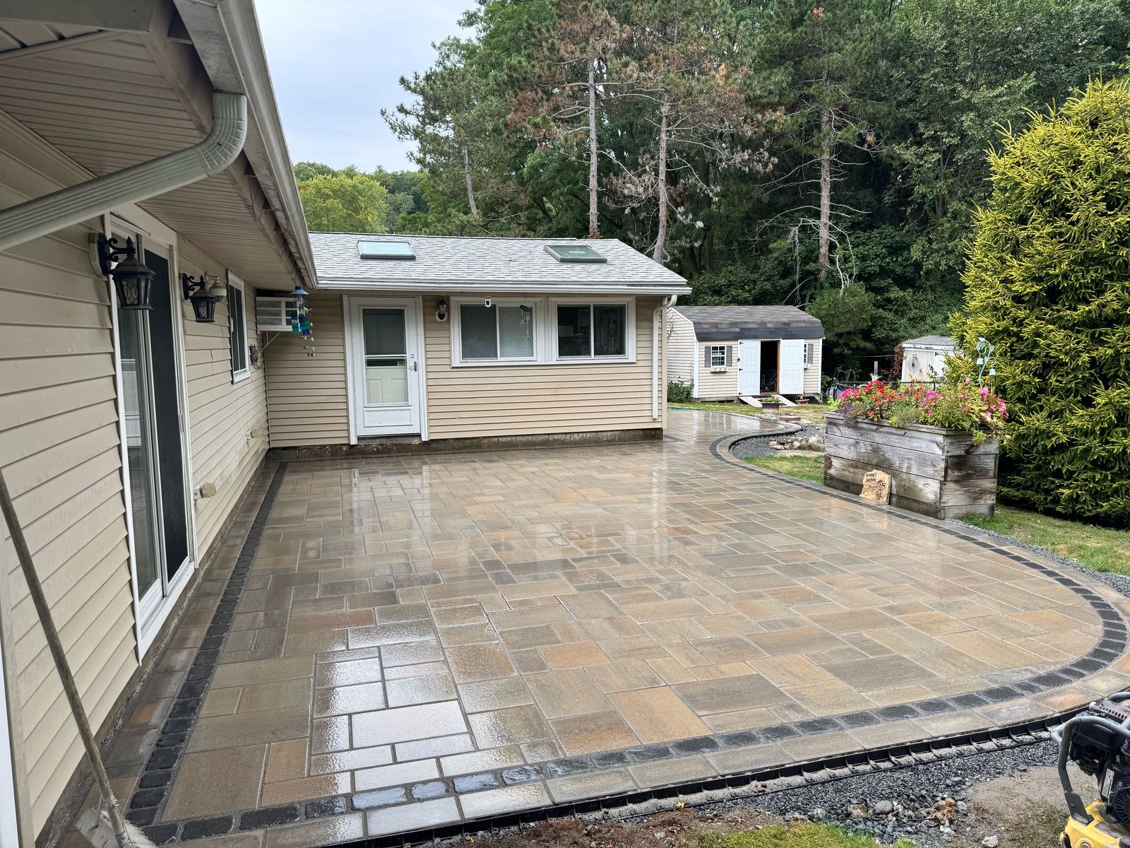 Large paver patio with a dark border and curved edge built by MLC beside a house and shed